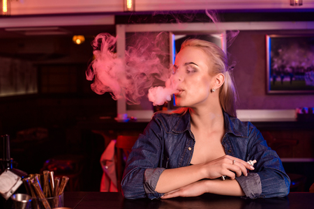 Young pretty woman smoke an electronic cigarette at the vape barの写真素材
