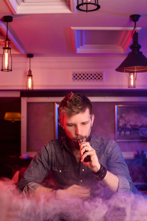 Vape. Vaping man in a cloud of vapor. Photo is taken in a vape bar.の写真素材