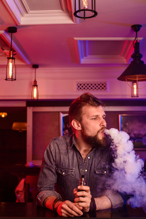 Vape. Vaping man in a cloud of vapor. Photo is taken in a vape bar.の写真素材