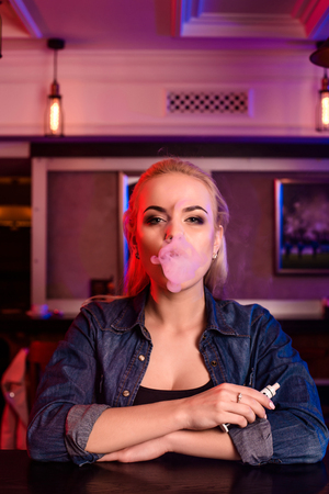 Young pretty woman smoke an electronic cigarette at the vape barの写真素材