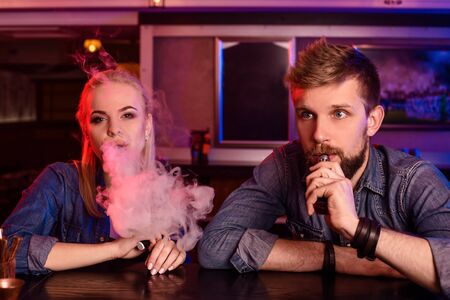 A man and woman smoking electronic cigarette in a vape bar.の写真素材