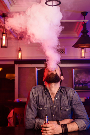 Vape. Vaping man in a cloud of vapor. Photo is taken in a vape bar.の写真素材