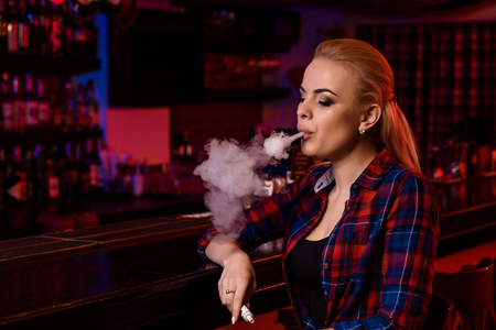 Young pretty woman smoke an electronic cigarette at the vape barの写真素材