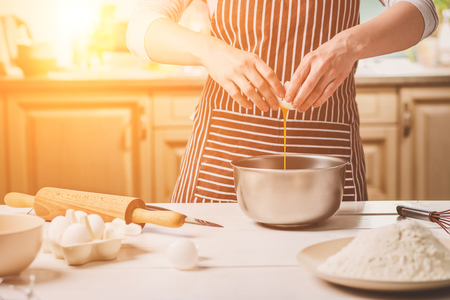 Young woman breaking egg over bowl with dough, close-upの写真素材