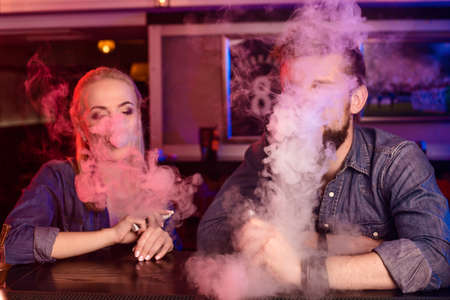 A man and woman smoking electronic cigarette in a vape bar.の写真素材