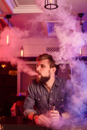 Vape. Vaping man in a cloud of vapor. Photo is taken in a vape bar.の写真素材