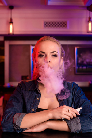 Young pretty woman smoke an electronic cigarette at the vape barの写真素材