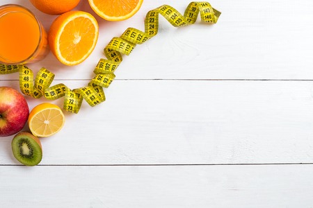 Fresh fruits with tape measure over white wooden background. Top viewの写真素材