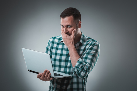 Frustrated businessman holding a laptop covers his face with his hand on gray background.の写真素材