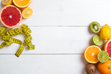 Fresh fruits with tape measure over white wooden background. Fitness concept. Top view. Copy space Flat layの写真素材
