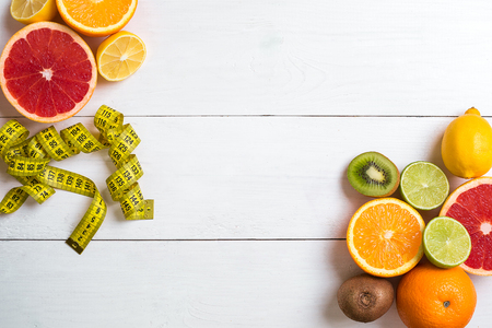 Fresh fruits with tape measure over white wooden background. Fitness concept. Top view. Copy space Flat layの写真素材