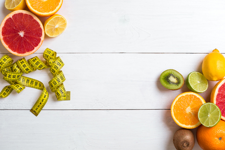 Fresh fruits with tape measure over white wooden background. Fitness concept. Top view. Copy space Flat layの写真素材