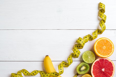 Fresh fruits with tape measure over white wooden background. Fitness concept. Top view. Copy space Flat layの写真素材