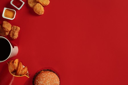 Concept of mock up burger, potatoes, sauce, chicken nuggets and drink on red background. Copy space for text and logo.の写真素材
