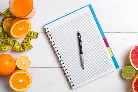 Fresh juice in glass from citrus fruits - lemon, grapefruit, orange, notebook with pencil on white wooden backgroundの写真素材