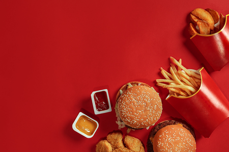 Two hamburgers and french fries, sauces on red background. Fast food. Top view.の写真素材