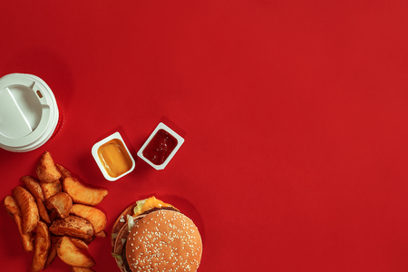 Concept of mock up burger, potatoes, sauce and drink on red background. Copy space for text and logo.の写真素材