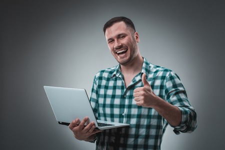 Portrait of young handsome man using laptop, wearing plaid shirtの写真素材