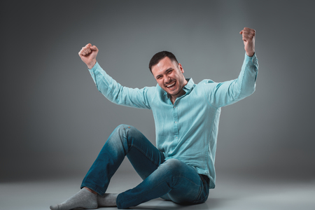 Appealing casual young man sitting on the floor, looking to the camera smilingの写真素材