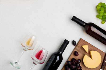 Two wine glasses with red and white wine,bottles of red wine and white wine, cheese on white background. Horizontal view from the top.の写真素材