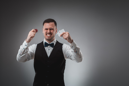 Young man in shirt and waistcoat shows his cards and holds poker chips in his hands, studio shotの写真素材