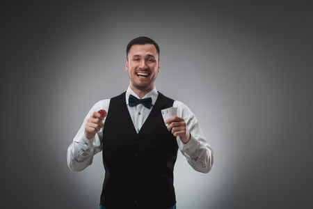 Young man in shirt and waistcoat shows his cards and holds poker chips in his hands, studio shotの写真素材