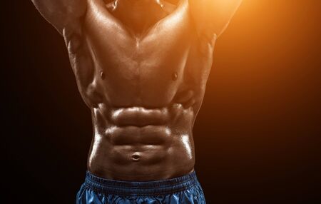 Muscular and fit young bodybuilder fitness male model posing over black background. Studio shot on black background. with sun flare. close-upの写真素材