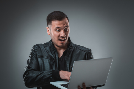 Man in black jacket looking at laptop, half turn. Holding opened laptop and working. Emotion.の写真素材