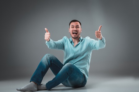 The man is sitting on the floor on gray background. Man showing different emotions.の写真素材