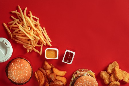Burger and Chips. Hamburger and french fries in red paper box. Fast food on red background. Hamburger with tomato sauce. Top view, flat lay with copyspaceの写真素材