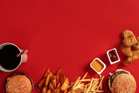 Burger and Chips. Hamburger and french fries in red paper box. Fast food on red background. Hamburger with tomato sauce. Top view, flat lay with copyspaceの写真素材