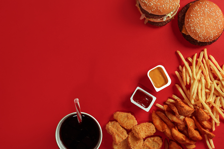 Fast food dish top view. Meat burger, potato chips and glass of drink on red background. Takeaway composition.の写真素材