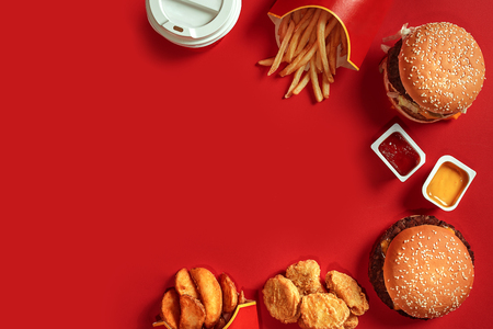 Fast food dish top view. Meat burger, potato chips and glass of drink on red background. Takeaway composition.の写真素材