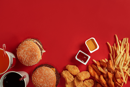 Fast food dish top view. Meat burger, potato chips and glass of drink on red background. Takeaway composition.の写真素材