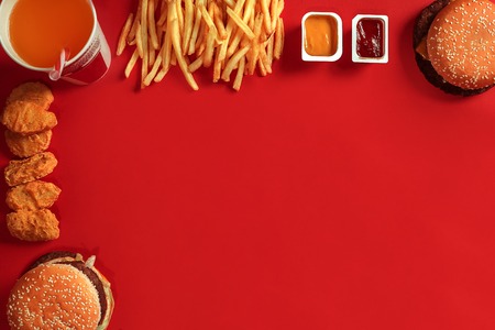 Fast food dish top view. Meat burger, potato chips and glass of drink on red background. Takeaway composition.の写真素材