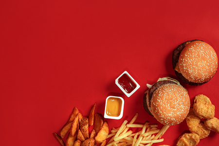 Fast food dish top view. Meat burger, potato chips and nuggets on red background. Takeaway composition.の写真素材