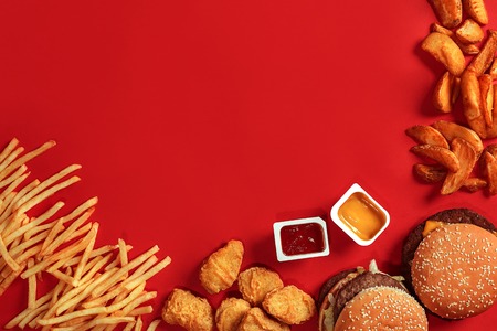 Fast food dish top view. Meat burger, potato chips and nuggets on red background. Takeaway composition.の写真素材