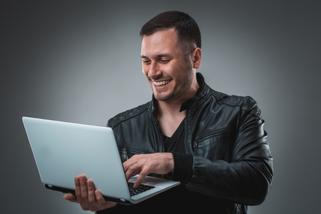 Man in black jacket looking at laptop, half turn. Holding opened laptop and working. Emotion.の写真素材