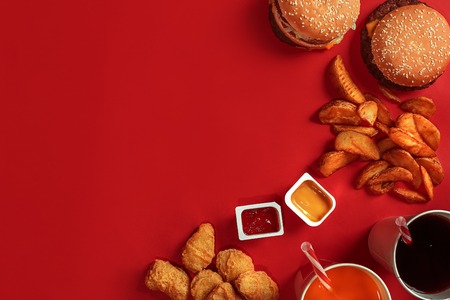 Fast food dish top view. Meat burger, potato chips and glass of drink on red background. Takeaway composition.の写真素材