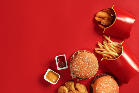 Fast food dish top view. Meat burger, potato chips and nuggets on red background. Takeaway composition.の写真素材
