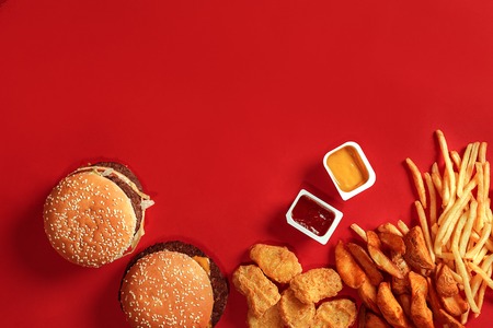 Fast food dish top view. Meat burger, potato chips and nuggets on red background. Takeaway composition.の写真素材