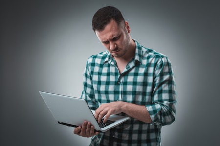 Attractive business man model in green shirt isolated on gray working with laptop, showing something by left hand. Caucasian guy.の写真素材