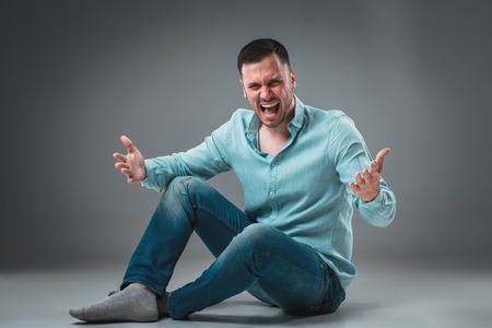 The man is sitting on the floor, isolated on gray background. Man showing different emotions.の写真素材