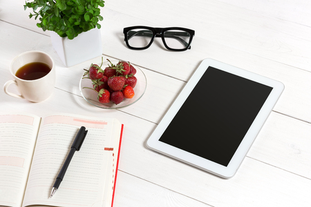 Office table desk with set of supplies, white blank notepad, cup, pen, tablet, glasses, flower on white background. Top viewの写真素材