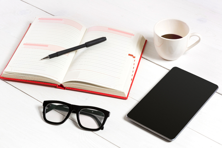 Office table desk with set of supplies, white blank notepad, cup, pen, tablet, glasses on white background. Top viewの写真素材