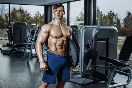 Handsome man with big muscles, posing at the camera in the gymの写真素材