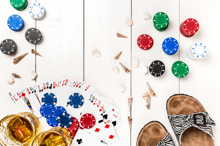 Card deck surrounded by poker chips and scattered seashells on white wooden background with copy spaceの写真素材