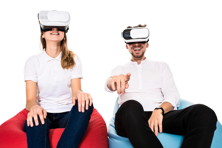 Excited young couple experiencing virtual reality seated on beanbags isolated on white backgroundの写真素材
