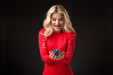 Young beautiful emotional woman with chips in hands on a black background in the studio. Pokerの写真素材