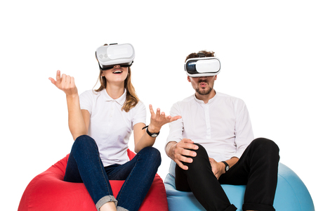 Excited young couple experiencing virtual reality seated on beanbags isolated on white backgroundの写真素材